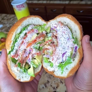 California BLT chopped bagel halves stacked and cut open, filled with bacon, avocado, lettuce, and tomato on a wooden board.