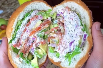 California BLT chopped bagel halves stacked and cut open, filled with bacon, avocado, lettuce, and tomato on a wooden board.