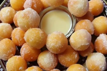 Golden fried donut holes dusted in sugar, freshly made and served warm on a white plate.