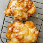 Close-up of two golden brown fresh peach fritters drizzled with vanilla glaze on a wire cooling rack.