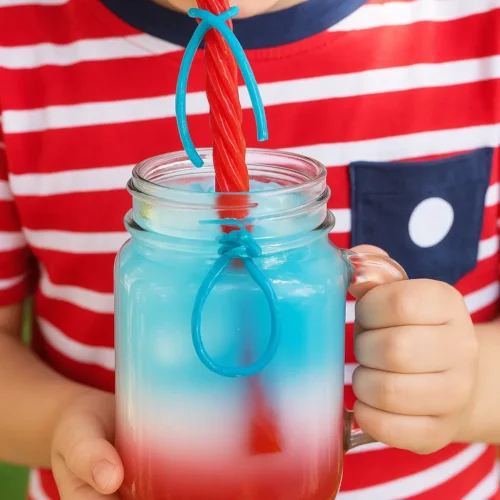 Child drinking kid-friendly patriotic punch from a mason jar using a Twizzlers licorice straw on the 4th of July