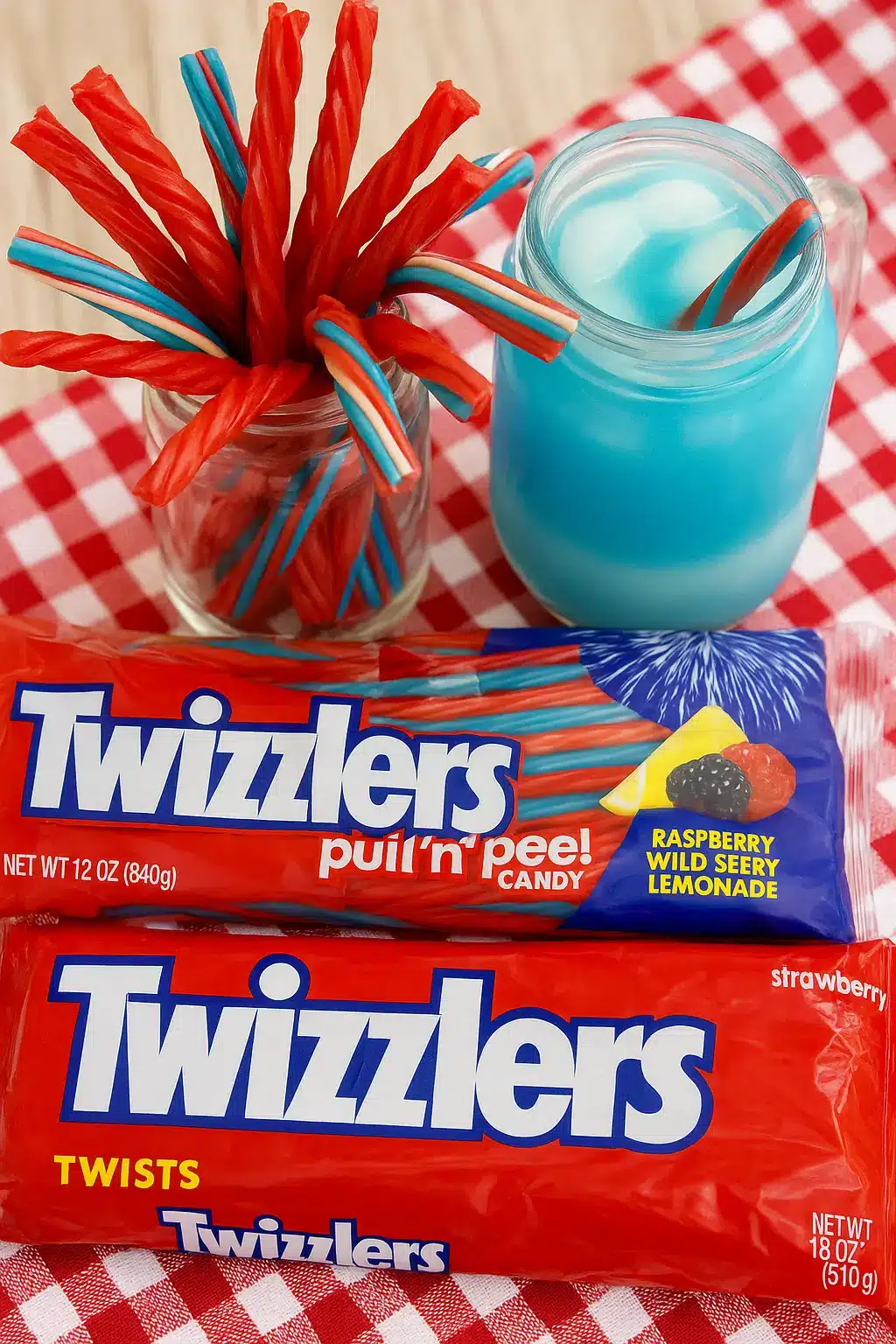Twizzlers red licorice and pull 'n' peel raspberry wild berry lemonade candy next to a blue patriotic drink on a red checkered tablecloth