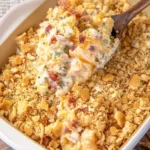Overhead view of Crack Chicken Casserole being scooped out of a casserole dish showing creamy texture, bacon, and golden cracker topping