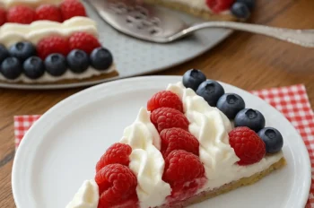 A slice of American Flag Fruit Pizza on a white plate with raspberries, blueberries, and whipped cream stripes
