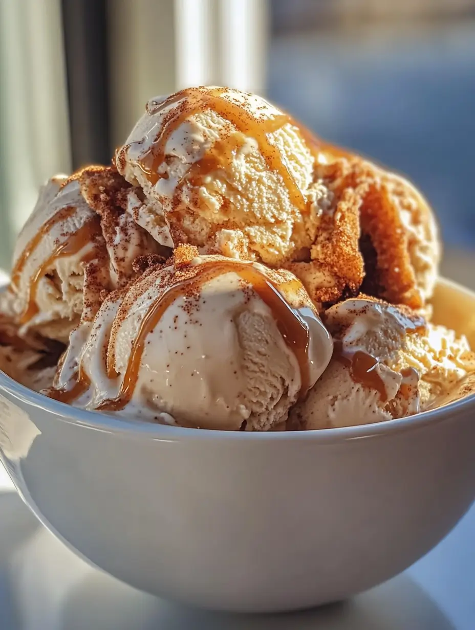 Scoops of Churro Cinnamon Delight Ice Cream in a white bowl, topped with cinnamon sugar, crispy churro pieces, and caramel drizzle in natural sunlight.