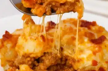 Close-up of a fork lifting a cheesy, bacon cheeseburger tater tot casserole with melted cheese strands.