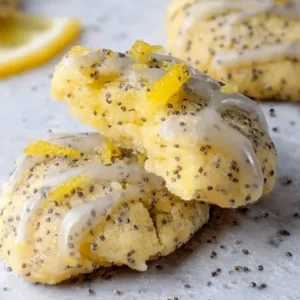 Soft lemon poppy seed cookies with lemon curd filling, drizzled with lemon glaze and sprinkled with poppy seeds, displayed on parchment paper.