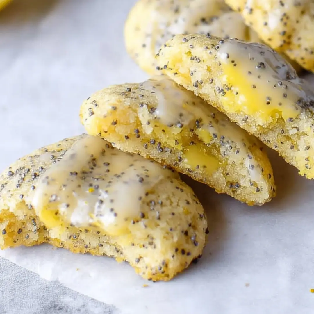 Stacked lemon cookies with poppy seeds and a bright lemon in the background, showcasing the vibrant citrus filling.