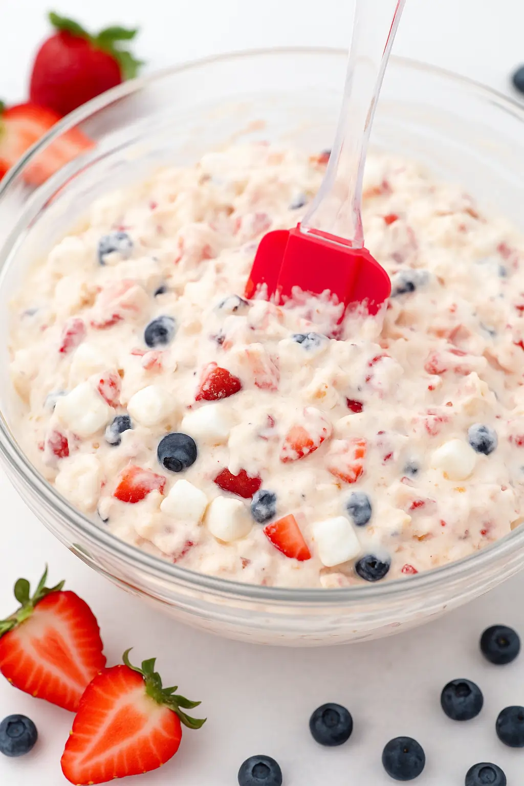 Red White and Blue Cheesecake Salad served in a large white bowl, garnished with fresh strawberries and blueberries on a table.