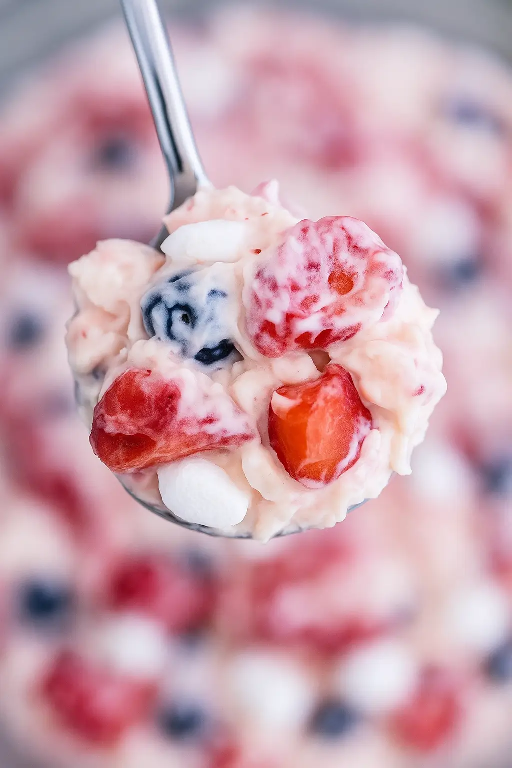 Spoonful of creamy Red White and Blue Cheesecake Salad featuring blueberries, sliced strawberries, and mini marshmallows.