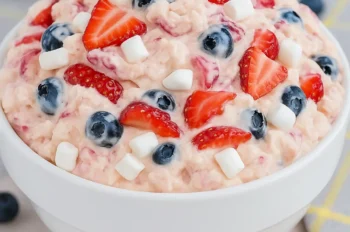 Close-up overhead view of Red White and Blue Cheesecake Salad in a white bowl, filled with strawberries, blueberries, and mini marshmallows.