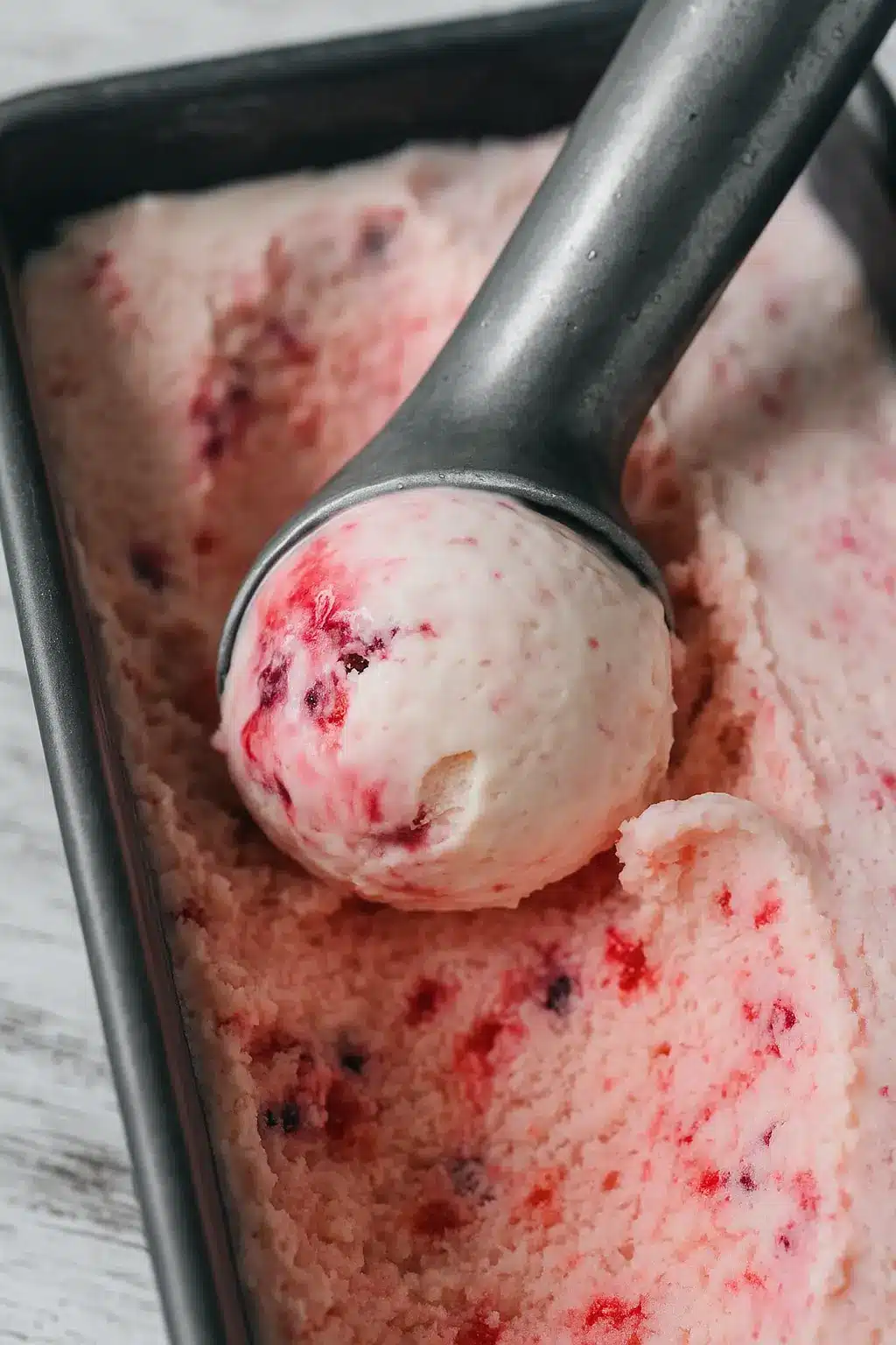 Scoop of rhubarb berry no churn ice cream in a loaf pan with visible fruit swirls