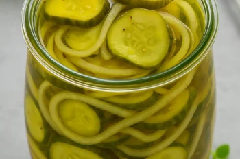 Glass jar filled with bread and butter pickles and sliced onions in golden brine on a gray background