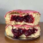 Front view of two brioche donuts stacked on a small silver tray, sliced to reveal a thick, juicy rhubarb-strawberry jam filling with bright pink glaze dripping slightly over the edges.