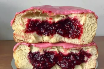 Front view of two brioche donuts stacked on a small silver tray, sliced to reveal a thick, juicy rhubarb-strawberry jam filling with bright pink glaze dripping slightly over the edges.