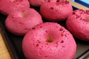 Close-up of six bright pink raspberry sourdough bagels on a black baking tray, showing their smooth, fluffy texture and rich color.