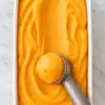 Creamy homemade peach sorbet being scooped from a white container
