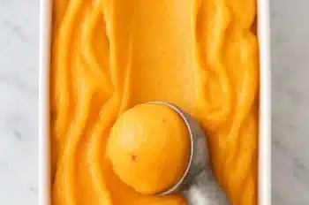 Creamy homemade peach sorbet being scooped from a white container