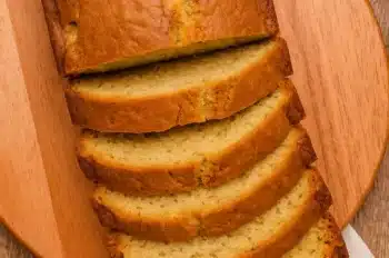 Sliced Southern Peach Bread displayed on a wooden board next to a small bowl of cream cheese or butter.