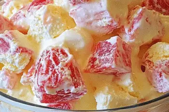 Side view of a layered Rhubarb & Custard Eton Mess in a glass bowl, showing fluffy meringue, rich custard, and ruby-red rhubarb