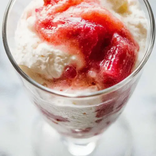 Close-up of rhubarb fool dessert with swirled whipped cream and rhubarb compote in a glass with a spoon.